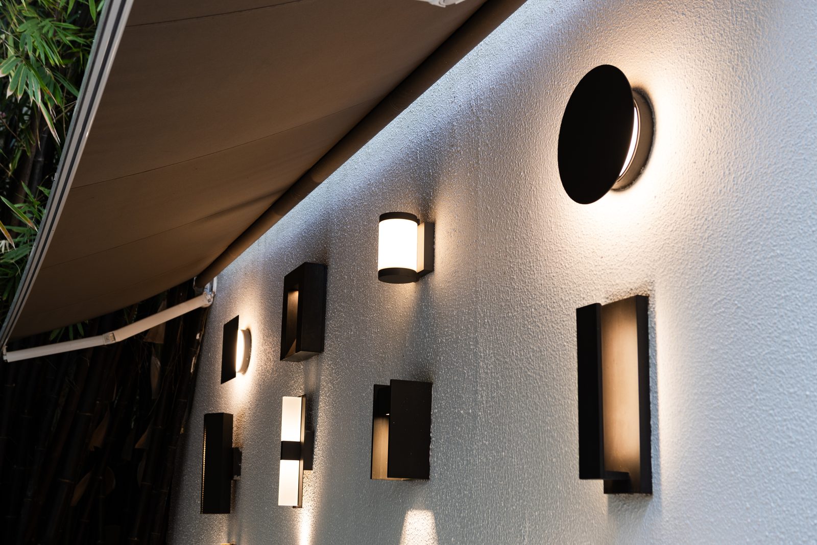 Outdoor wall with dark bronze exterior sconces lit at dusk under an awning